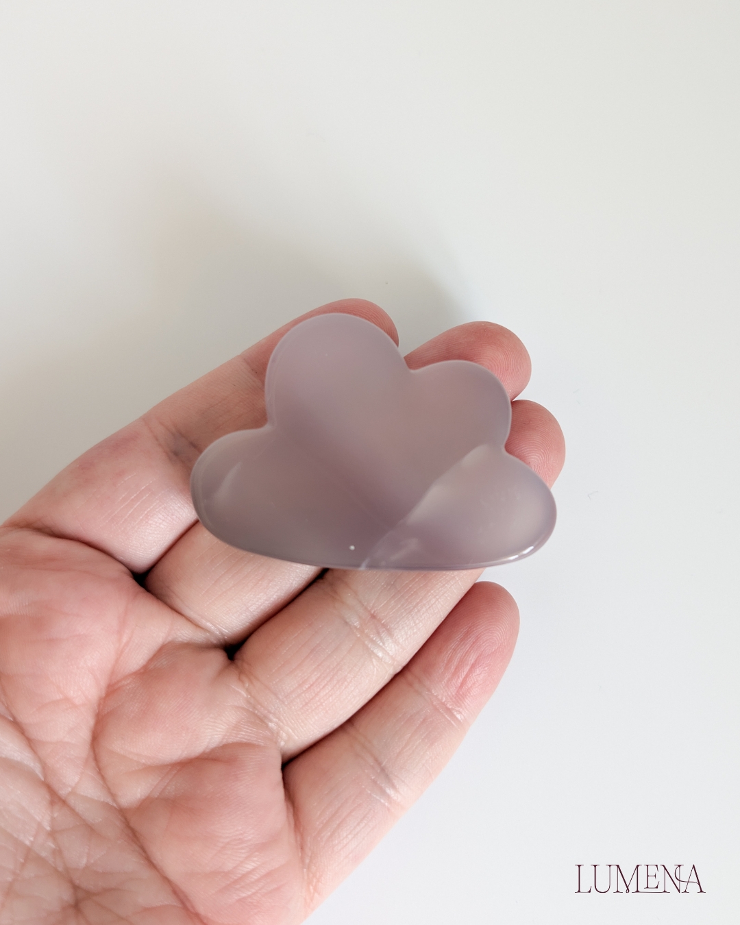 Image shows a hand holding a grey agate crystal carved into a cloud shape