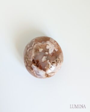 Image shows a flower agate pebble. It has lots of blossom-like patterns and is various shades of peach, white and cream