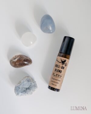 Image shows 4 crystals - an Angelite tumbled crystal, a Satin Spar (Selenite) mini sphere, a Smoky Quartz tumbled stone and a blue Celestite cluster placed in a semi-circle next to an Agnes + Cat aromatherapy blend roll on made with Chamomile, Lavender and Neroli essential oils