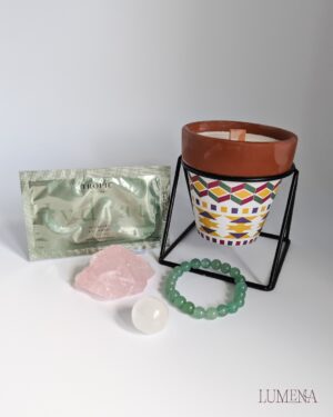 Image shows a candle in a terracotta pot, with an aztec design painted on. Next to the candle is a pack of Tropic Hydrogel Eye Masks, a rough rose Quartz, a green aventurine bead bracelet and a small Satin Spar (selenite) sphere. This kit has been put together to help you find a moment to pause in your day, to create calm, and to lighten the emotional load from the day.