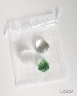 Image shows a small satin spar (selenite) crystal sphere, a clear quart tumble and a fluorite octahedron crystal collection, placed on a white table with a white organza bag.