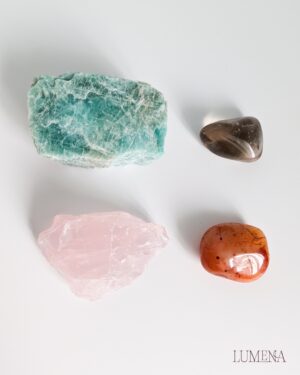 Image shows a raw Amazonite chunk, a raw rose quartz chunk, and a smoky quartz and carnelian tumbled crystal, all on a plain white background